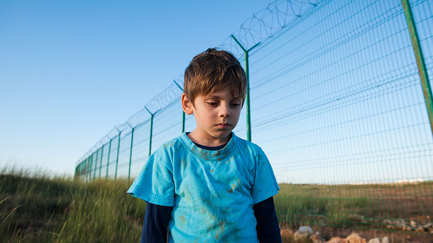Boy refugee walking along fence