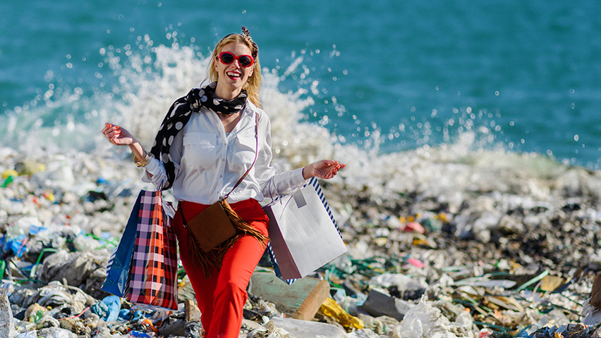 Woman standing on pile of  trash holding shopping bags at beach