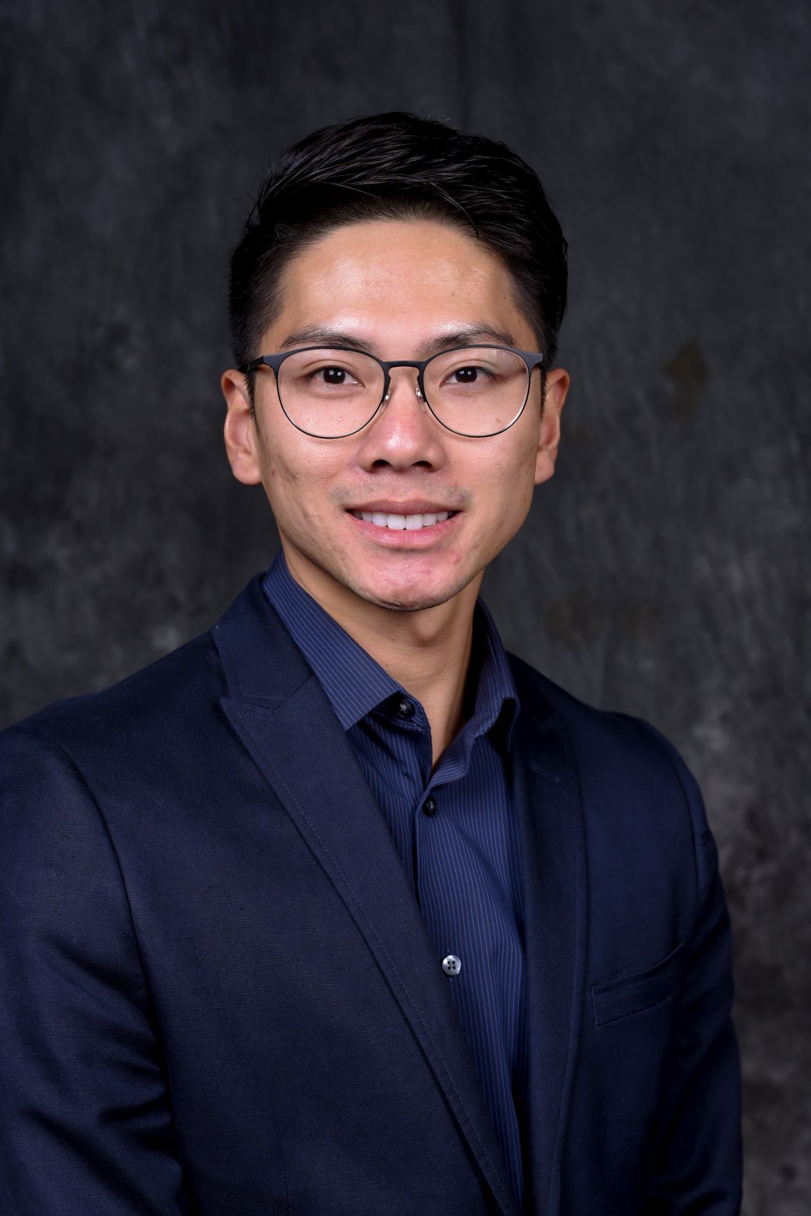 Headshot of APCC Director, Nathan Nguyen. Nathan is smiling, wearing glasses and a suit.