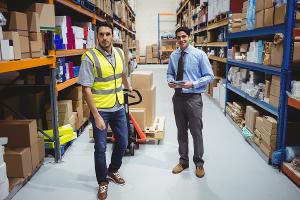 Male businessman purchasing product in warehouse with safety-vested worker towing dolly
