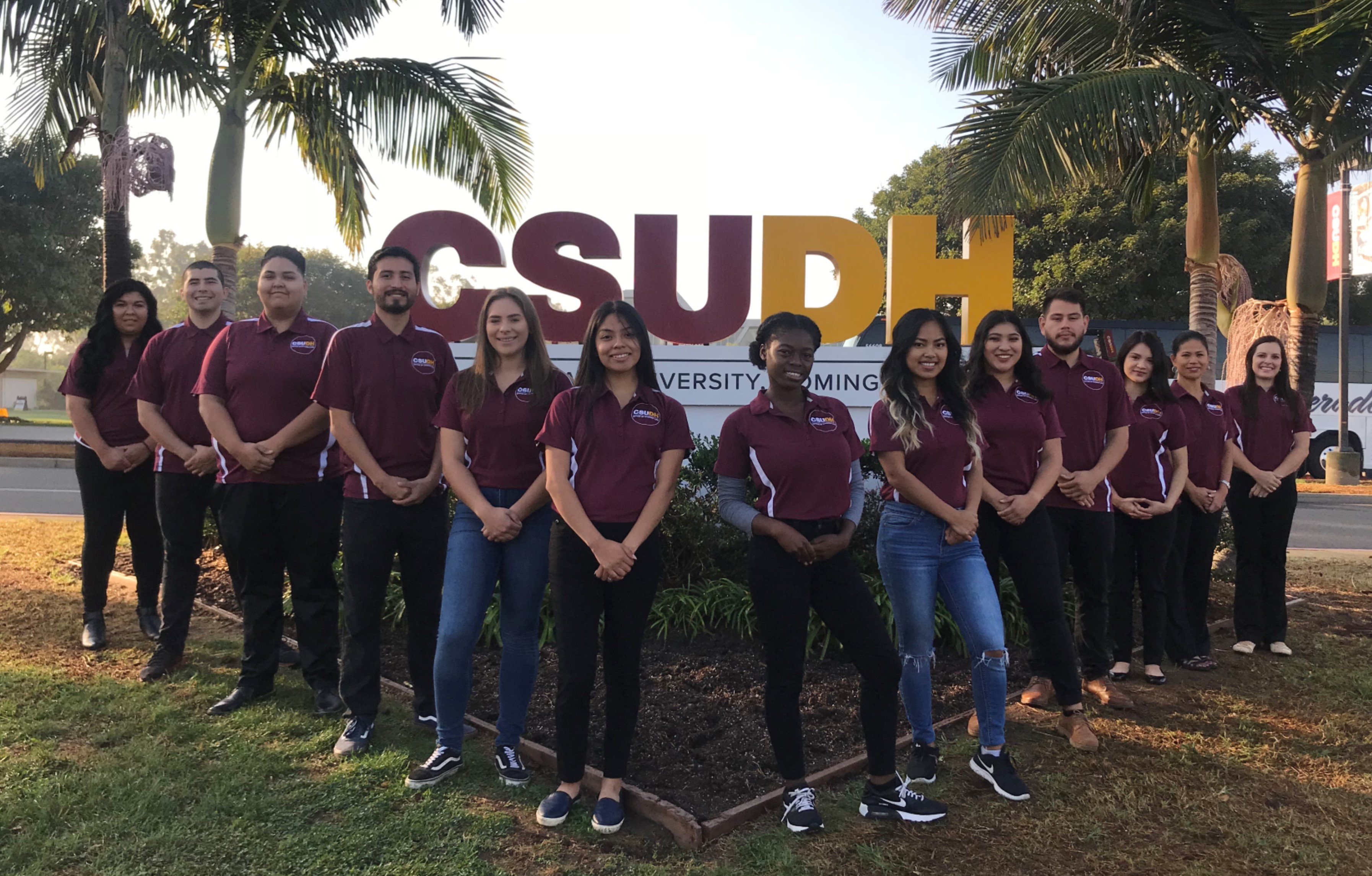 OSLStaffPicFall2018 A picture of all staff members who work in the Office of Student Life standing in front of the large CSUDH sign on Victoria Street.